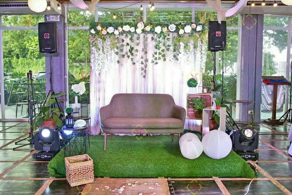 Wedding stage framed by greenery, speakers, uplights, and decorative lighting